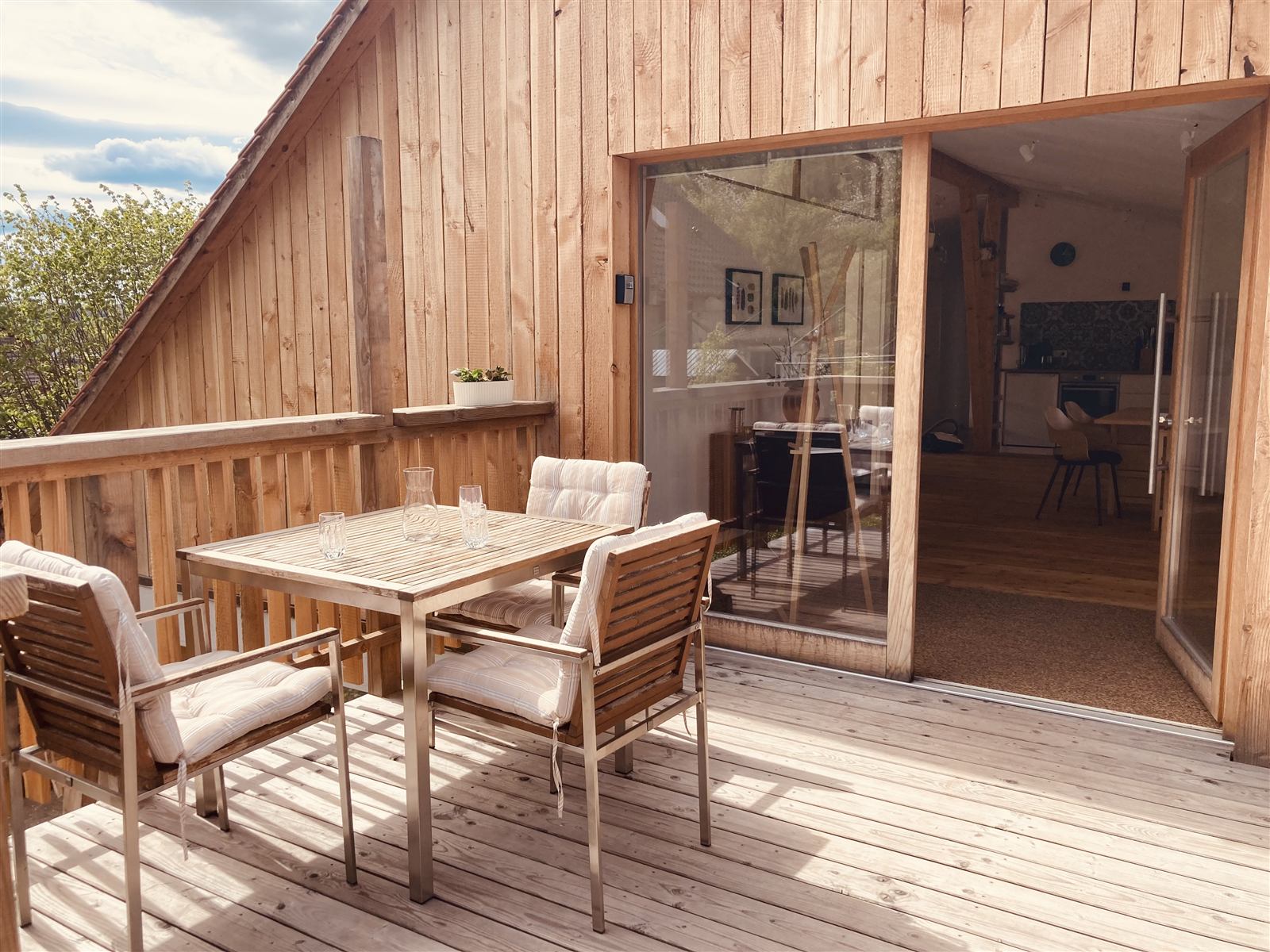 Holzterrasse vor der Ferienwohnung mit Tisch, Stühlen und großer Glastür